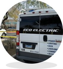 Rear of a white ECO ELECTRIC ambulance with emergency lights on top, parked on a street behind yellow caution tape, side lettering visible.