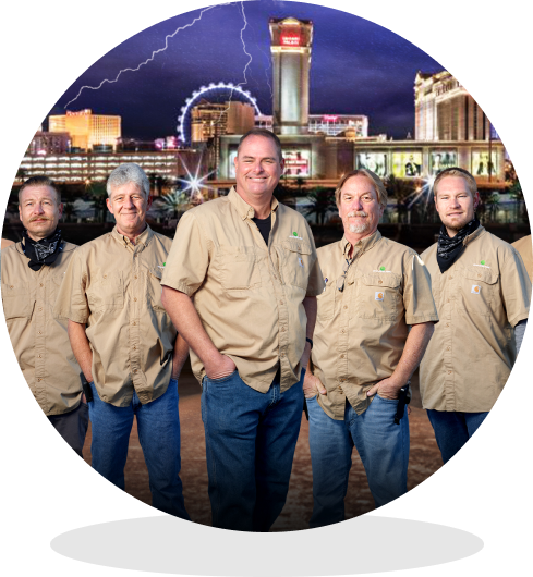 Five men in khaki shirts posing together outdoors, with a nighttime city skyline and lightning in the background.
