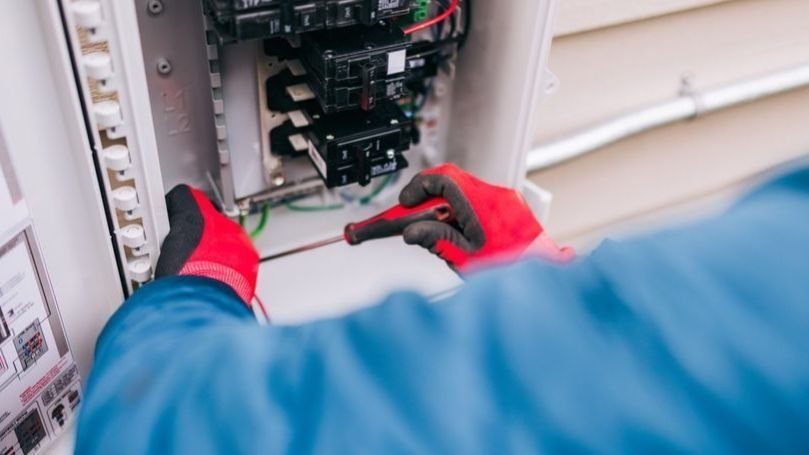 Electrician repairing electrical panel with gloves.
