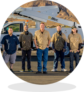 Five workers stand in a line in front of a utility bucket truck at a job site, posing for a team photo.