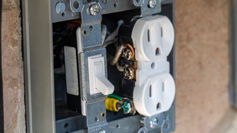 Switch next to an open outlet being installed into wall.