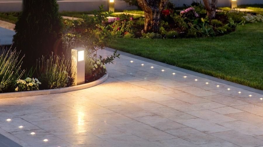 Evening scene of a stone patio with embedded ground lights along the edge and a well-kept garden bed nearby