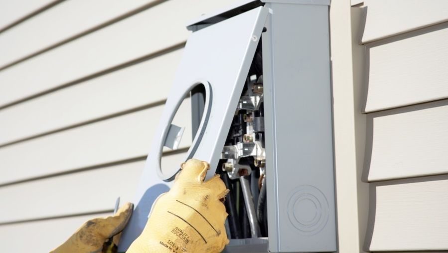 Worker opening an outdoor electrical panel to access wiring during a service or inspection.