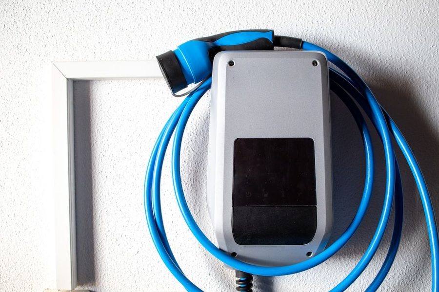 Wall-mounted electric vehicle charger with a bright blue charging cable coiled around it on a wall surface